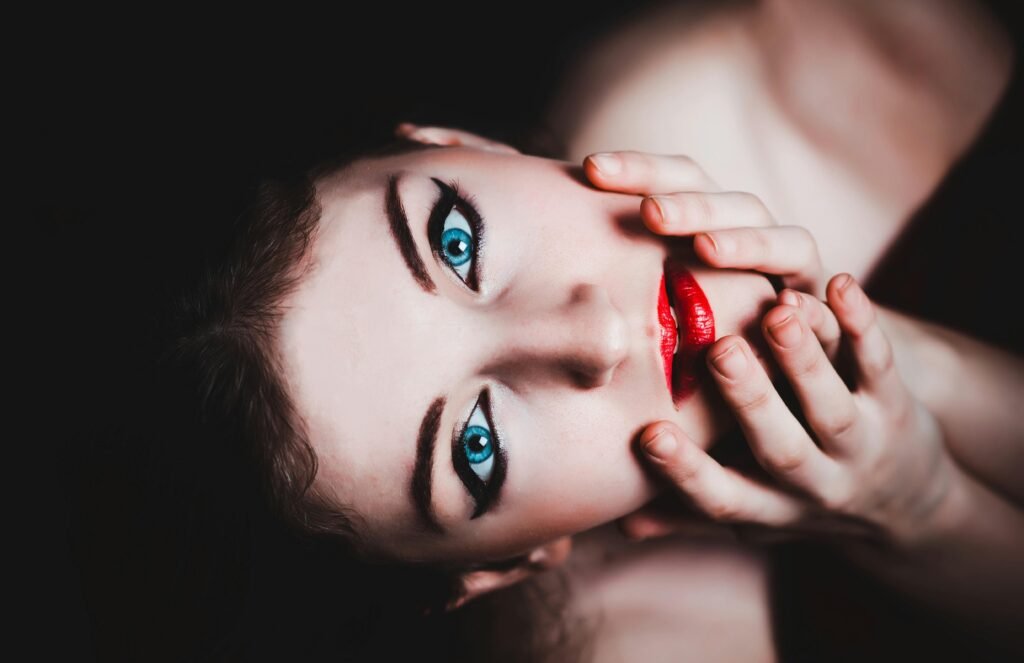 Close-up portrait of a woman with striking makeup, showcasing vivid blue eyes and red lips.